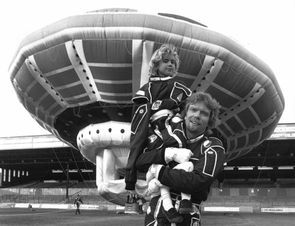 black and white photo of Richard Branson holding his daughter and standing in front of what looks like a UFO