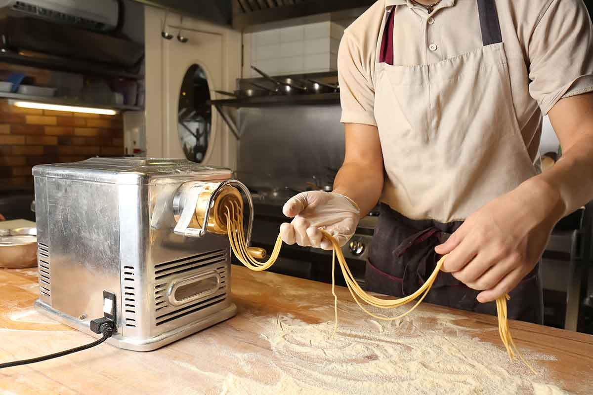 Man in apron holds spaghetti as it comes out of a pasta maker