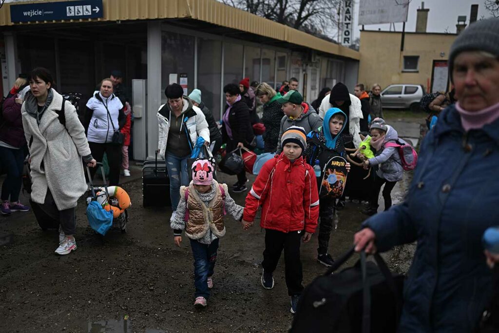 adults and children, many pulling luggage, walk outside of a train station