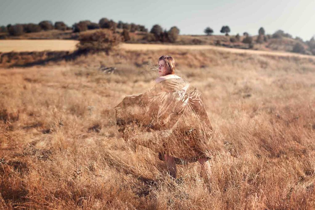 A person stands in a field dressed in material that makes her look partially invisible.