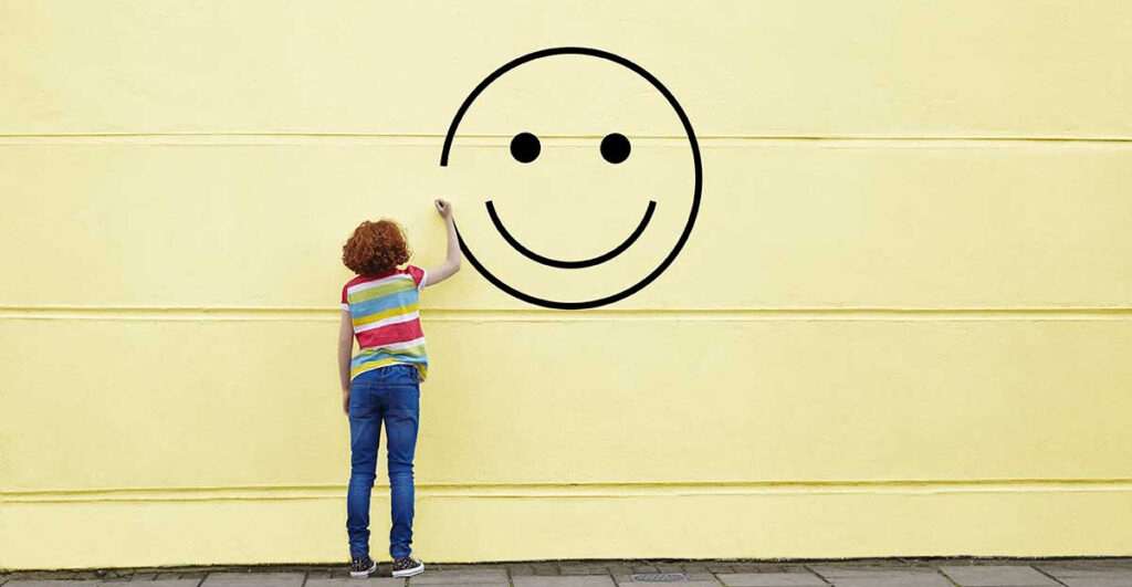 A child draws a happy face on a yellow wall