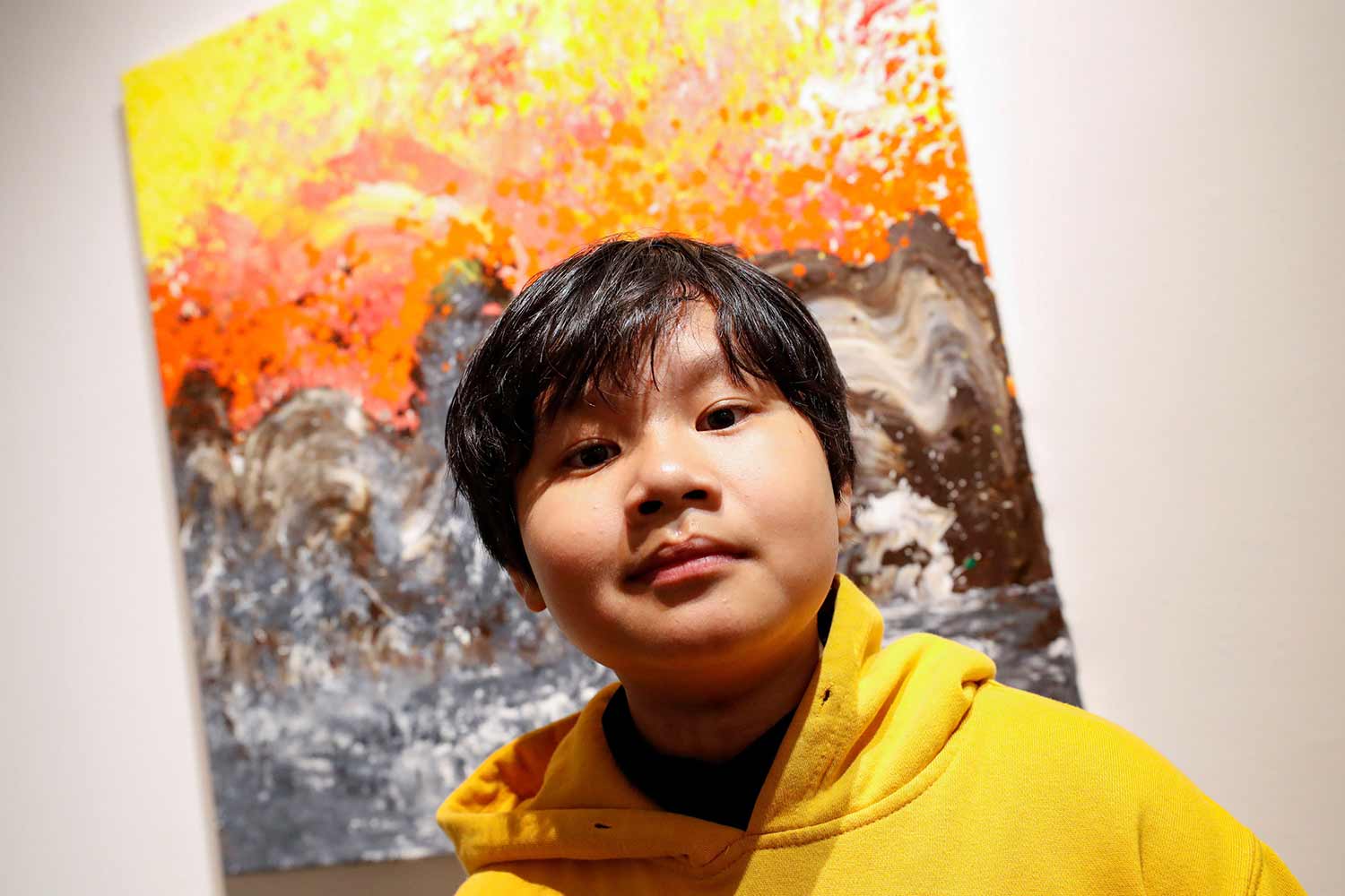 A young boy poses in front of a painting.