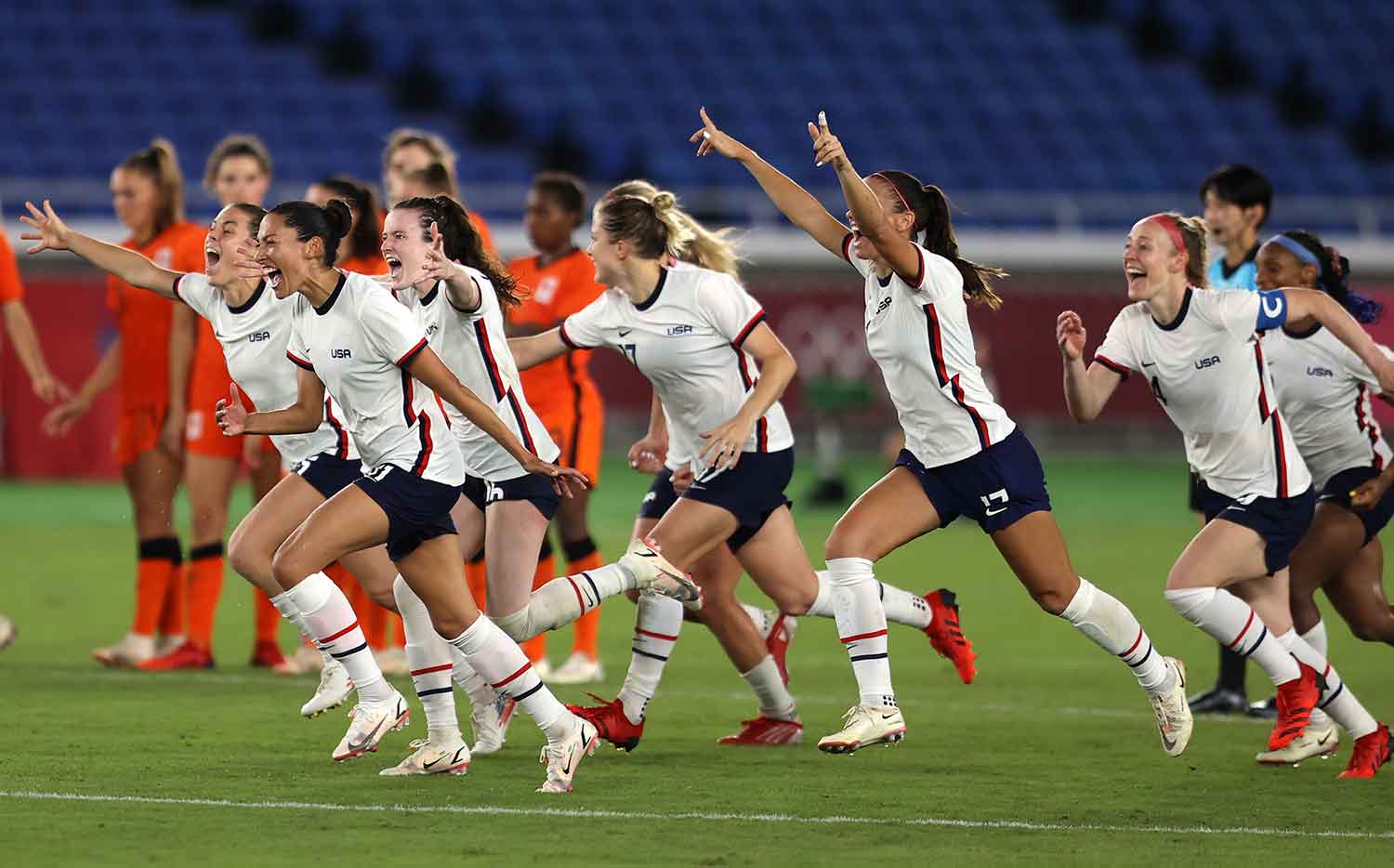 The U.S. women’s soccer team running and celebrating on a soccer field while another team looks on
