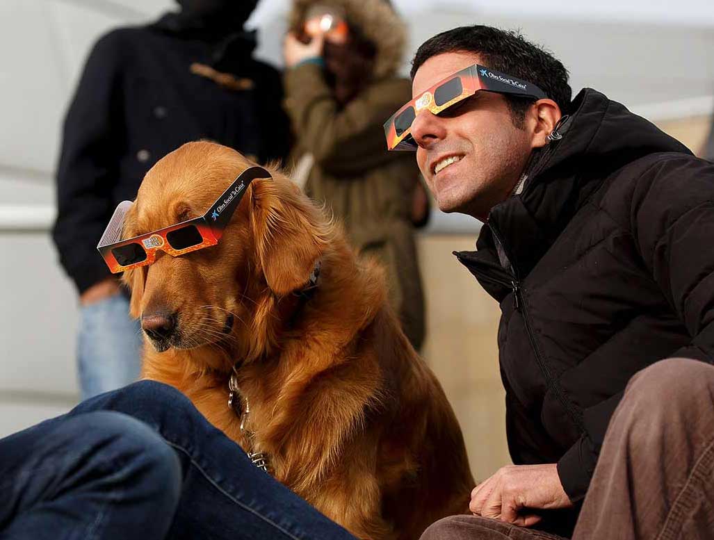A man and a dog wearing protective glasses during an eclipse