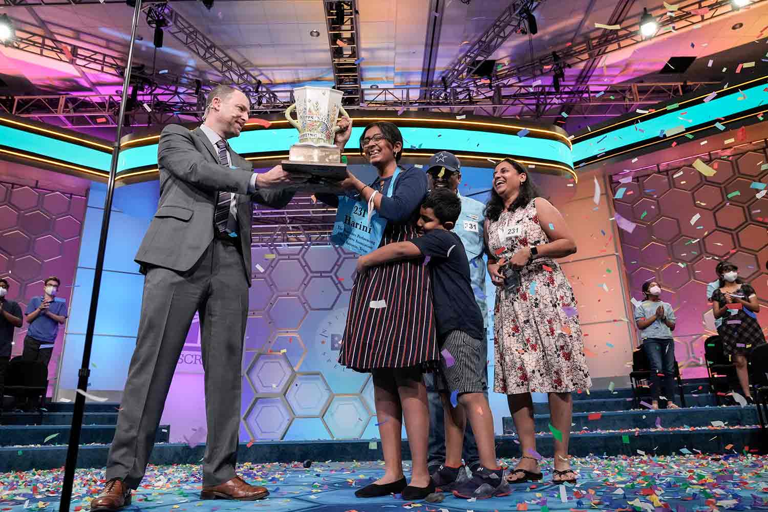 A teen girl smiles as she accepts a trophy from a man and gets a hug from a boy as her family surrounds her.