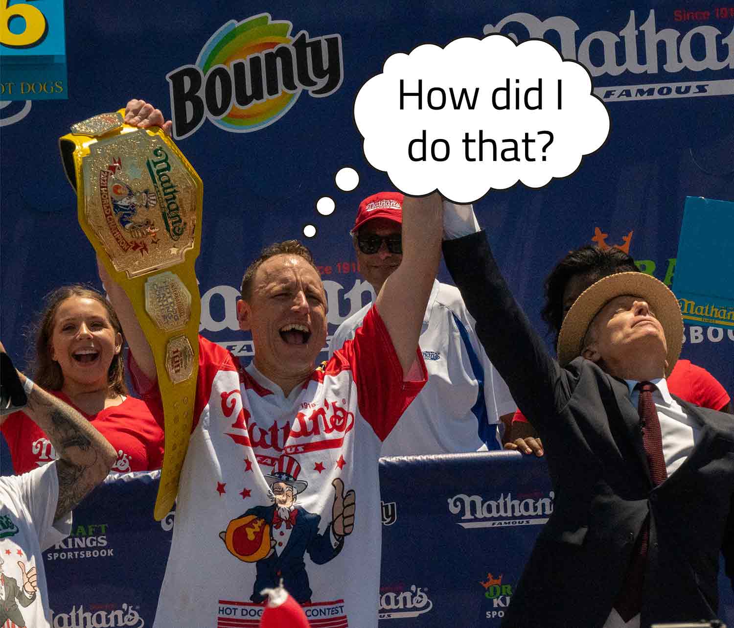 Joey Chestnut smiling and holding up a championship belt that says Nathan’s with a thought bubble that says How did I do that.