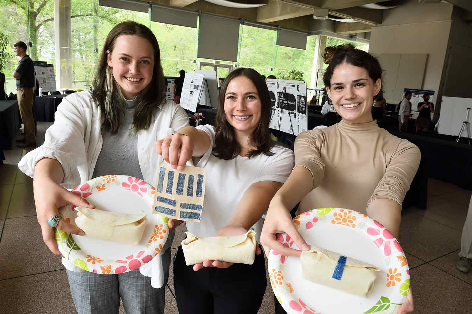 Three young women holding burritos that are fastened with tape