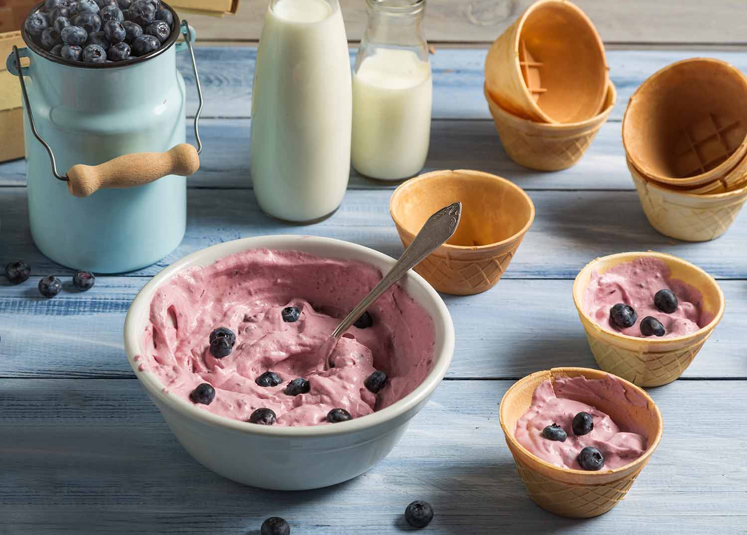 One large bowl and two small bowls of blueberry ice cream with other bowls and bottles of milk