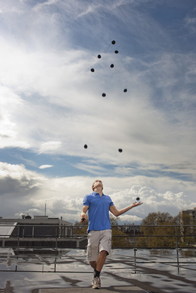 A young man stands outside and juggles 11 balls.
