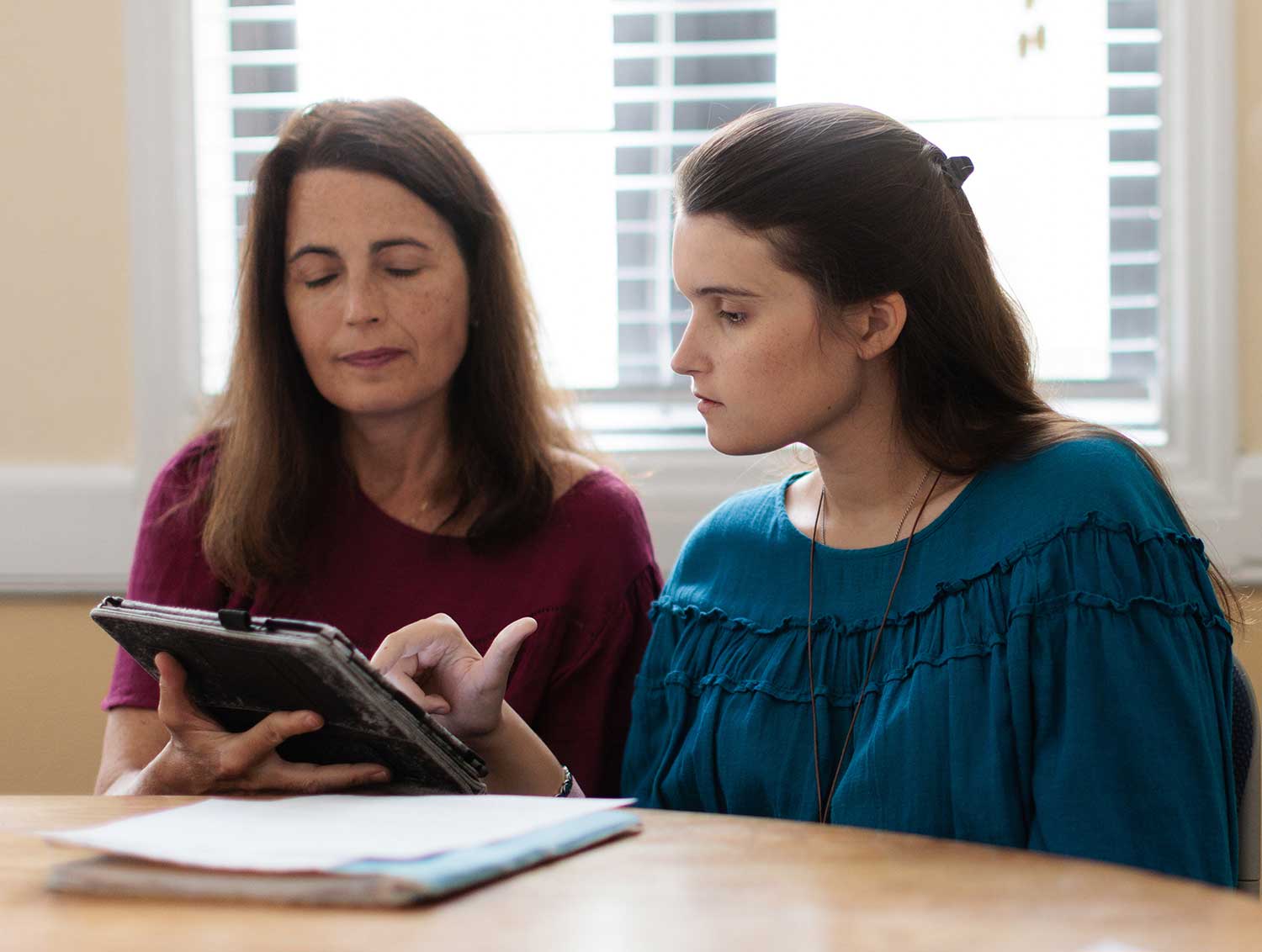 Two women sit at a table. One of the women holds a keyboard while the other types on it.