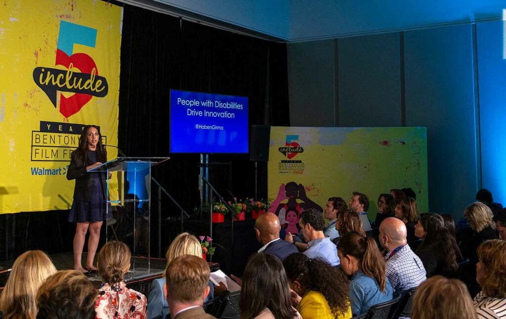 A woman stands at a podium and speaks before an audience.