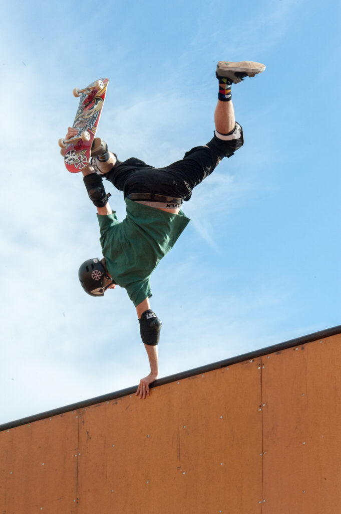 A skateboarder balances upside down holding onto a wall with one hand and his skateboard with the other