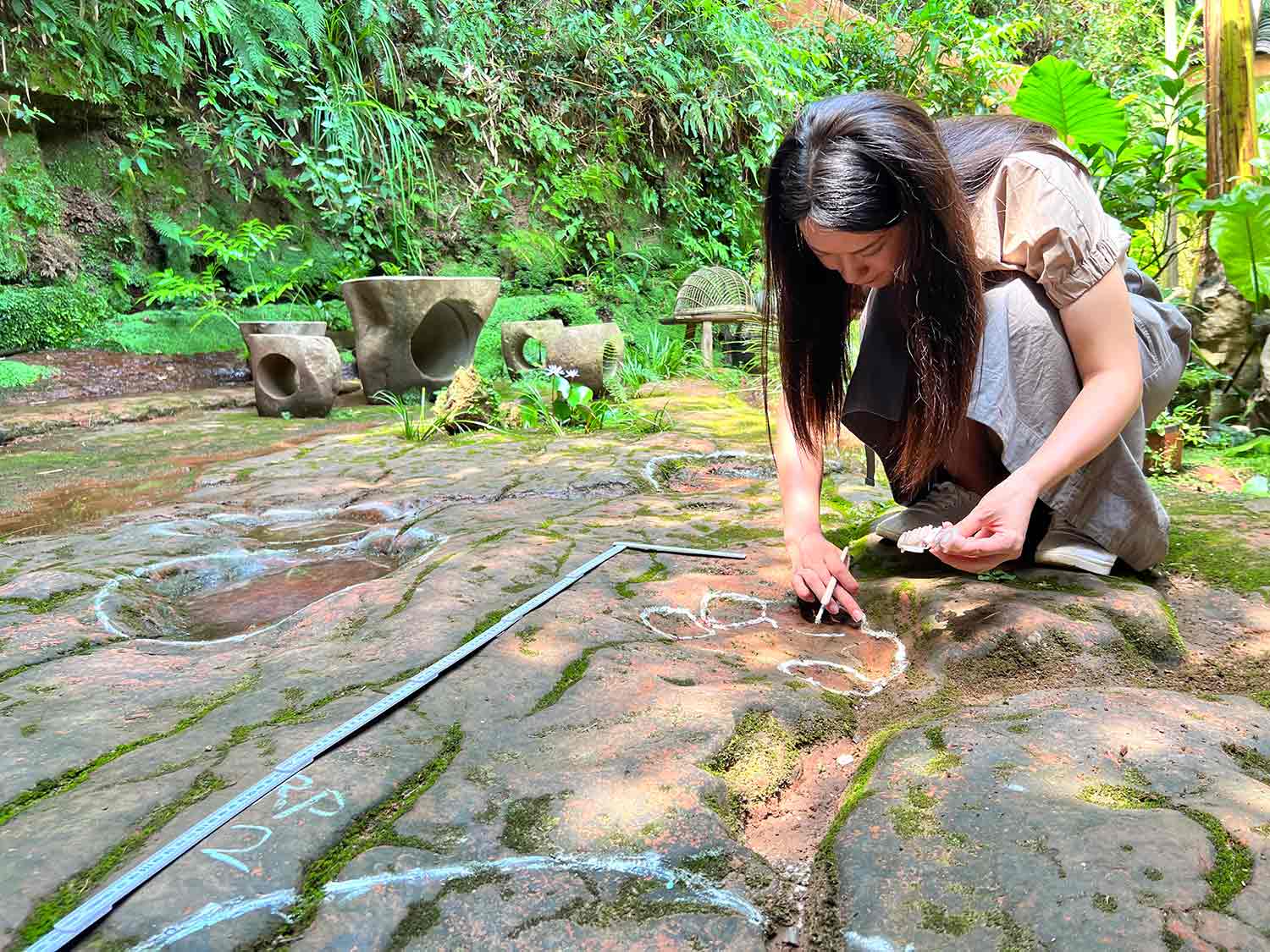 A woman outlines shapes on the ground in white and is surrounded by other shapes outlined in white.