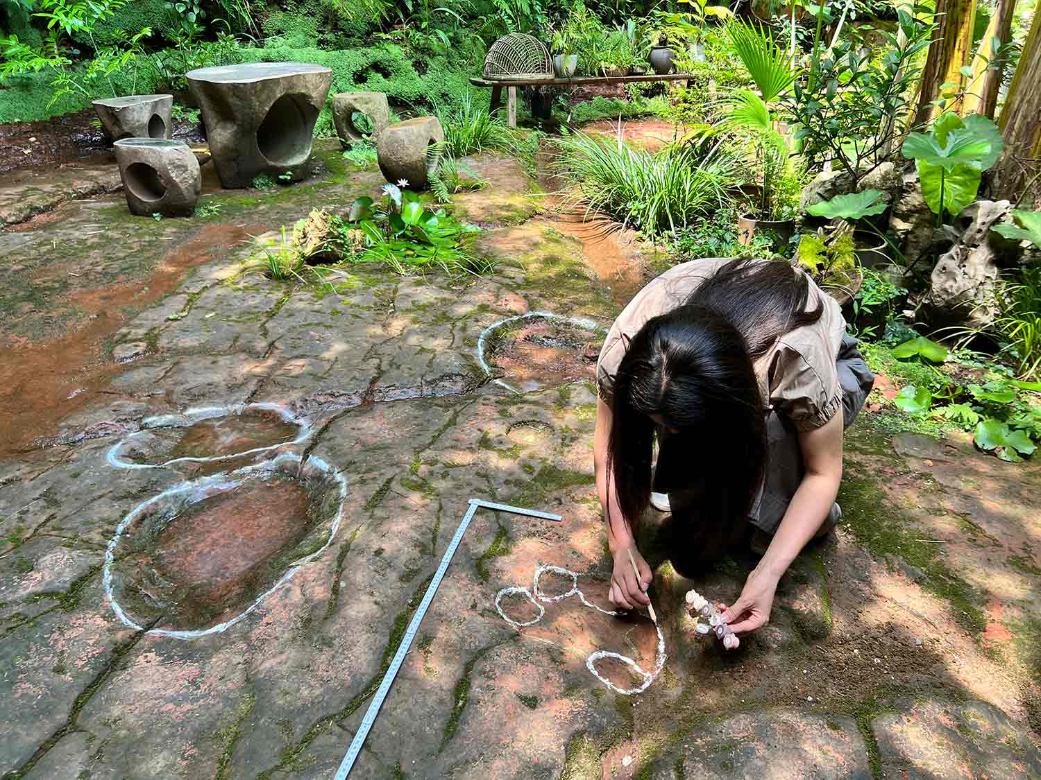 A woman outlines shapes on the ground in white and is surrounded by other shapes outlined in white.