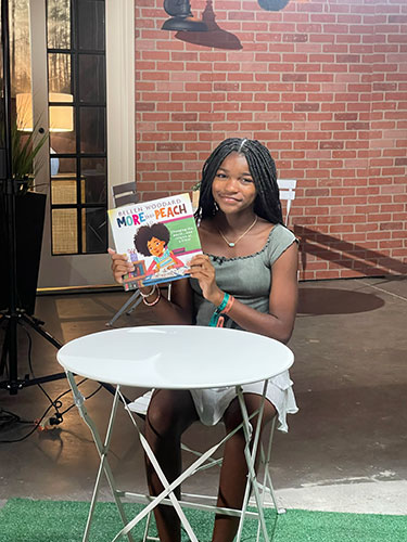 Bellen Woodard sits at a table holding up her book, More than Peach.