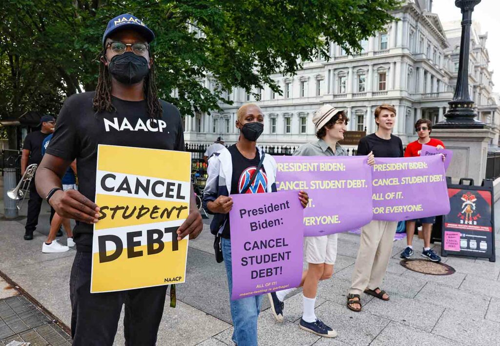 Five young people stand outside holding signs urging President Biden to cancel student debt.