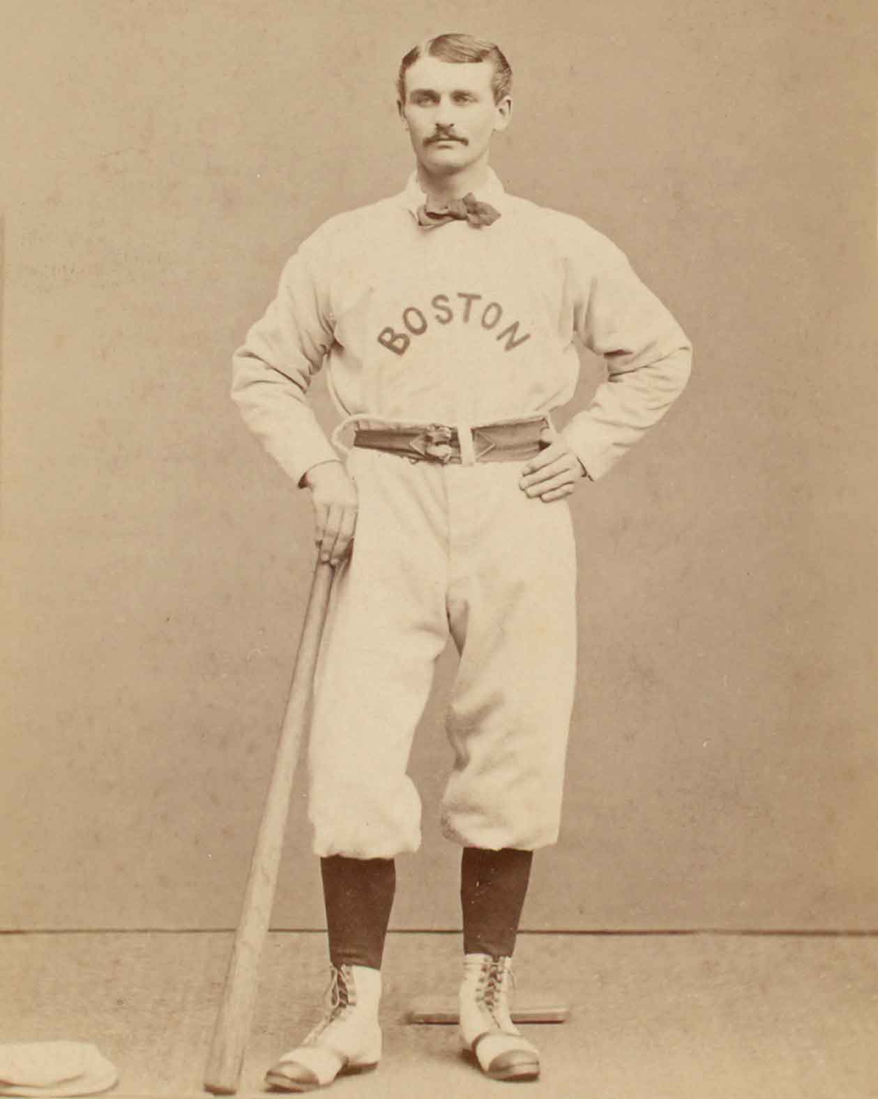 Black and white photo of a man posing with a bat and wearing a 19th century baseball uniform that says Boston.
