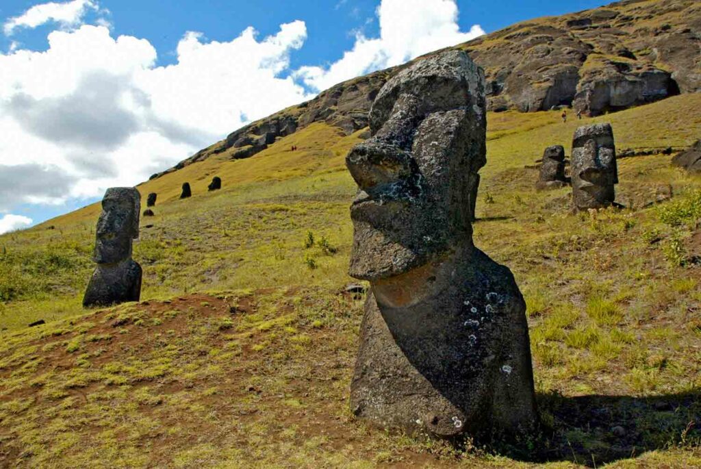 Large statues of heads stand on a green hillside.