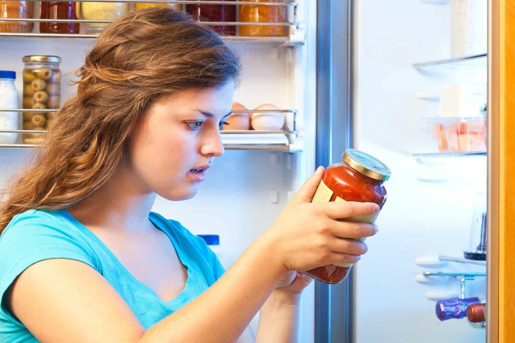 A teen girl has a worried expression on her face as she looks at a jar of sauce.