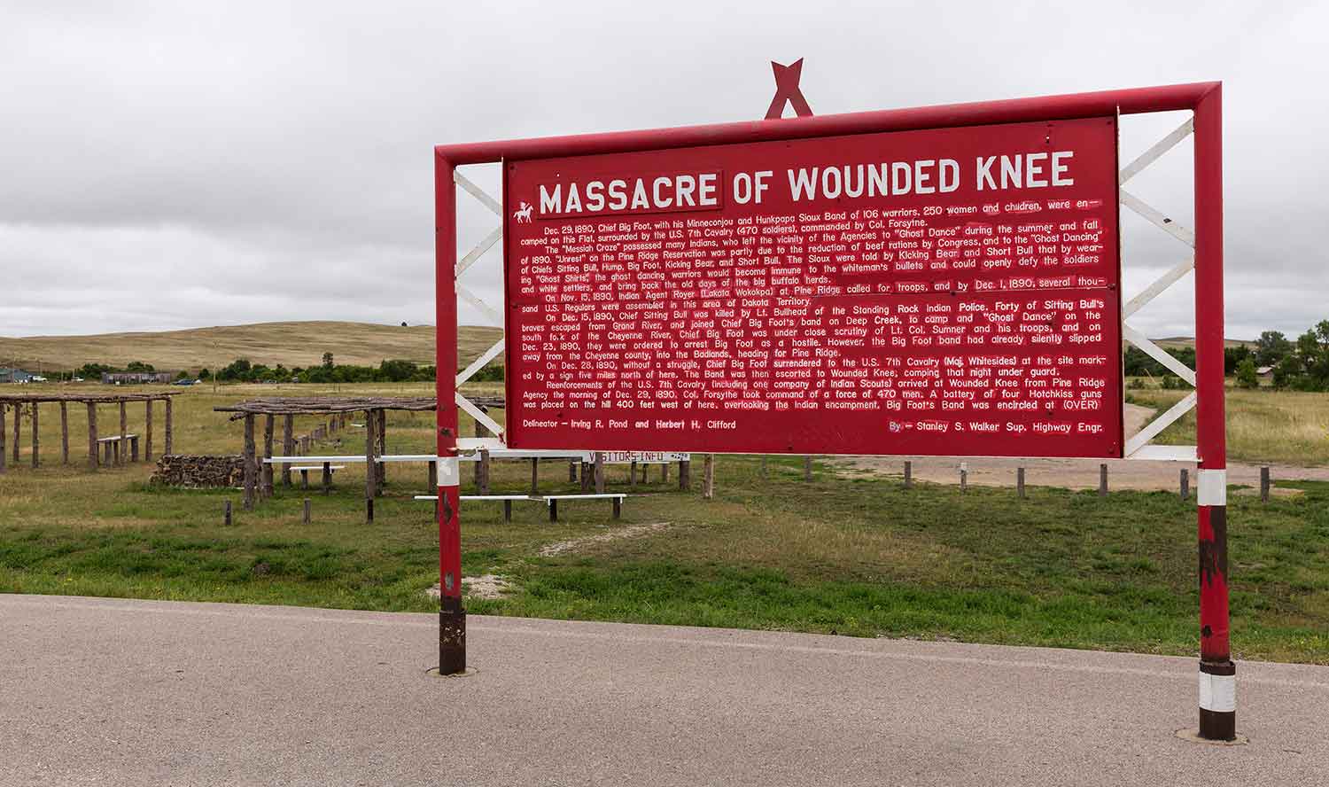 A plaque called Massacre of Wounded Knee tells the story of the massacre and stands in front of a hilly landscape.