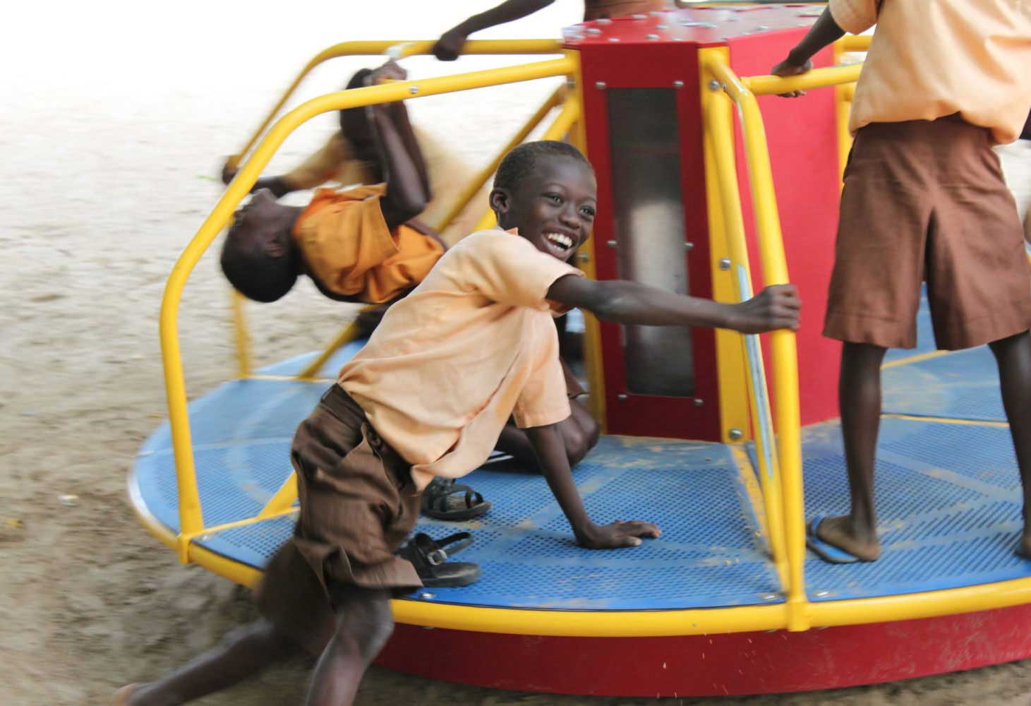 A boy smiles on a merry-go-round as he plays on it with other kids.
