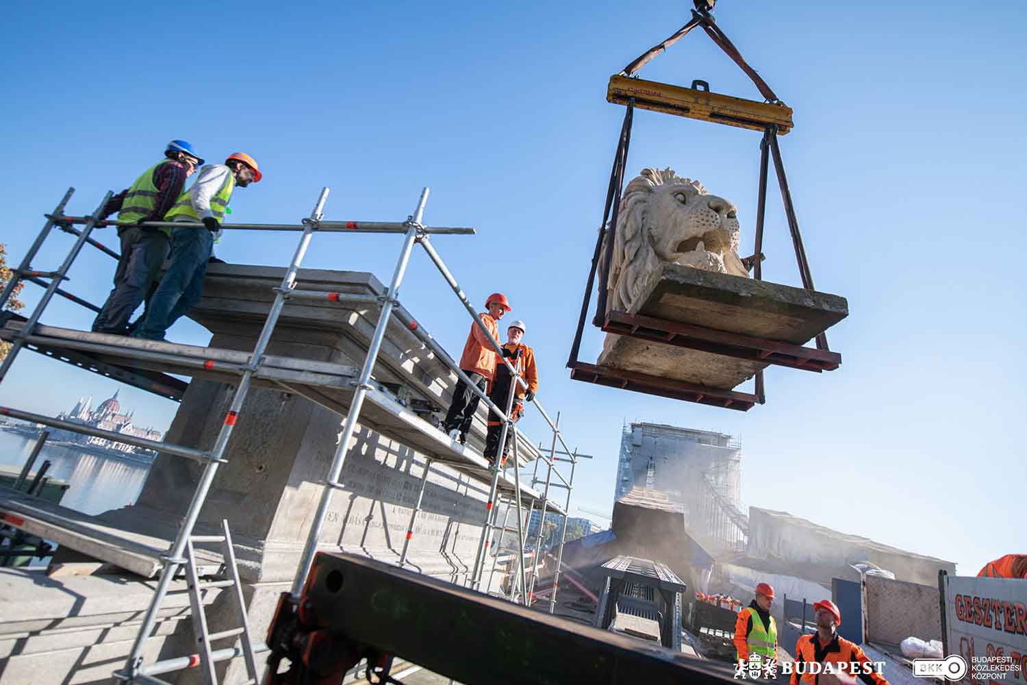 Construction workers on scaffolding watch as equipment is used to lift part of a stone lion