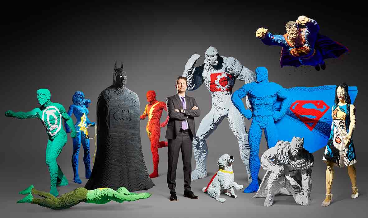 A man poses with 10 life-sized superheroes that are made of LEGO and a LEGO dog.