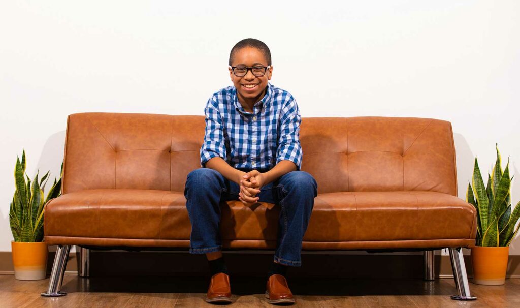 A boy poses and smiles while sitting on a couch.