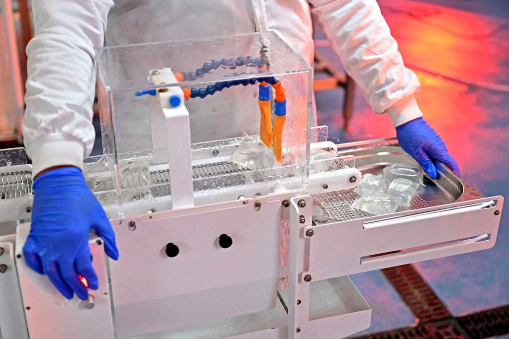 Two gloved hands hold either side of a manufacturing device that is producing plastic.