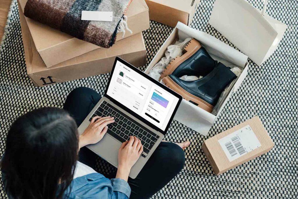 Overhead view of a woman using a laptop for online shopping and surrounded by packages of new items.