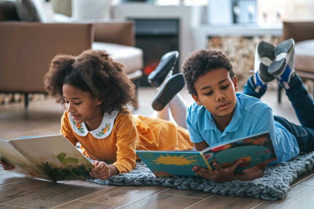 Two kids lie on the floor reading picture books.