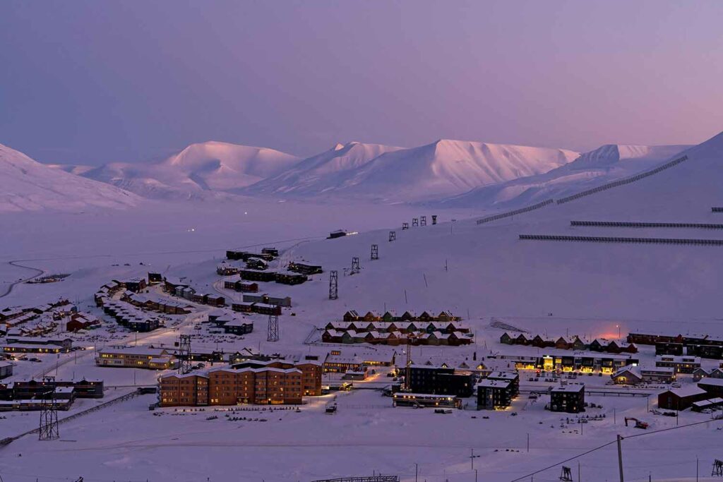 Buildings on a snow, mountainous landscape with a pinkish sky.
