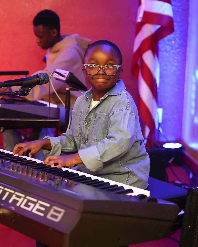 An 11-year-old boy sits at a keyboard and smiles.