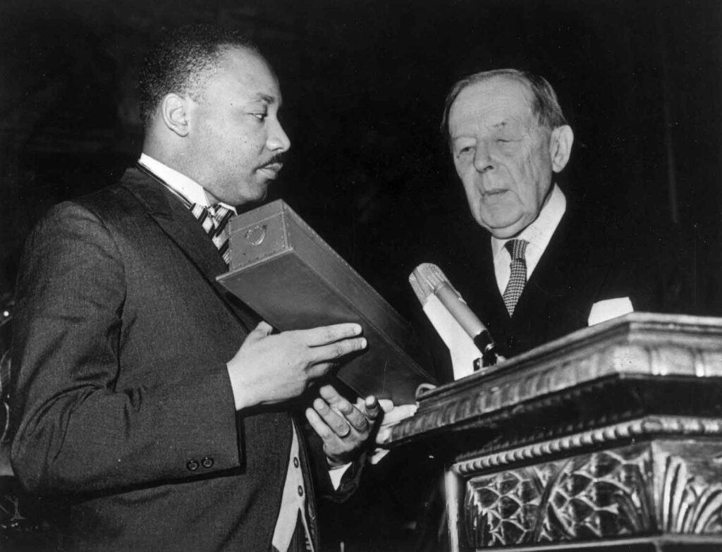 Martin Luther King and Gunnar Jahn stand at a podium as King holds a box and looks at Jahn.