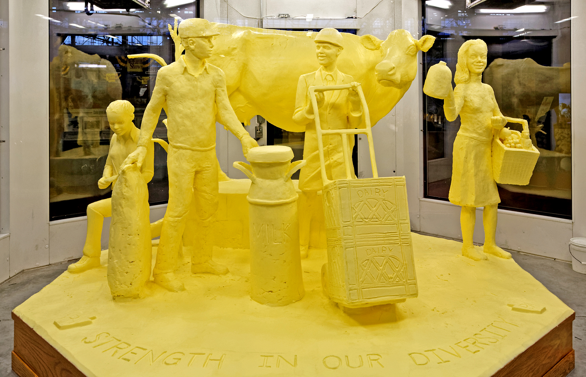 A large butter sculpture of a cow and two adults and two children who are doing dairy-related work.