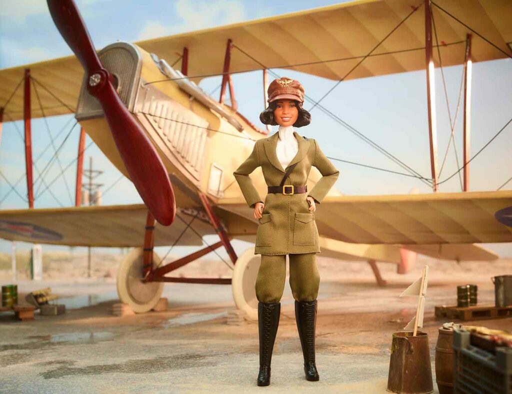 A doll in early 20th century aviator clothing stands in front of a toy propeller plane.