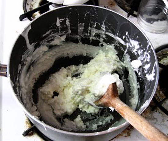 Thick and pasty white material in a black pot with a wooden spoon