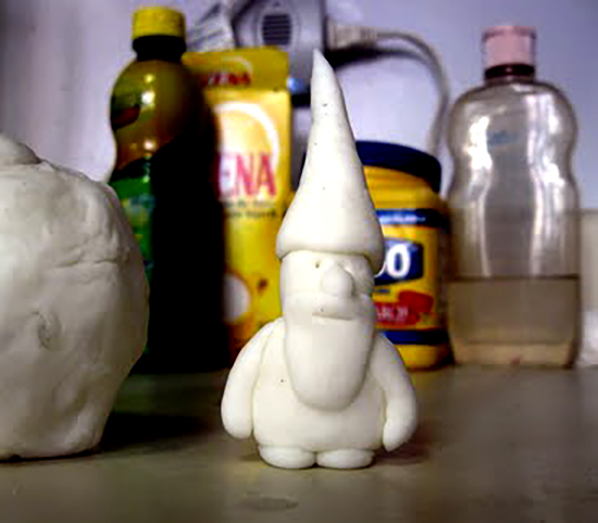 A small white clay gnome with some bottled kitchen products in the background
