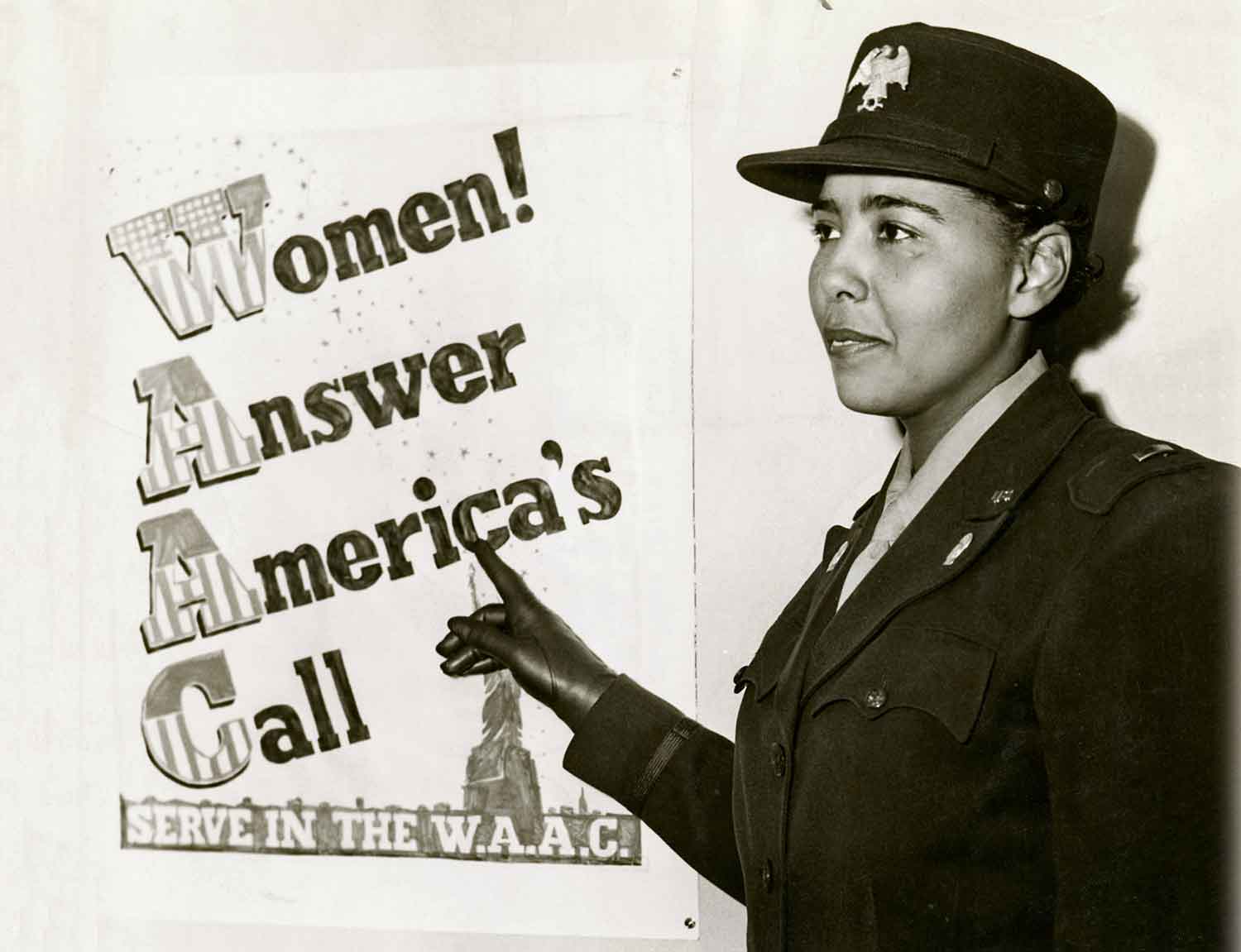A woman in a military uniform points to a poster that says Women Answer America’s Call.
