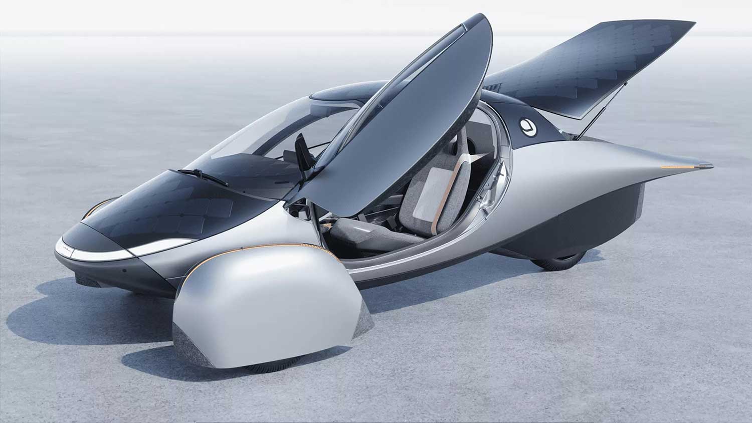 A three-wheeled black and silver car with solar panels sits on hard surface with door and trunk open