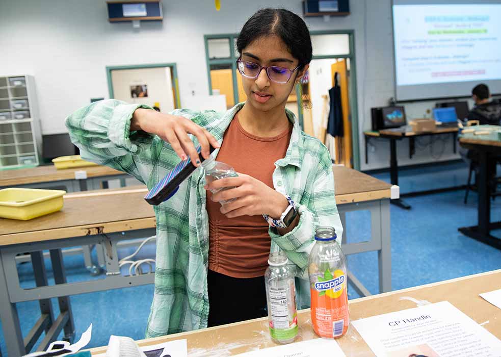 A teen uses a flat device to twist a cap off a bottle.