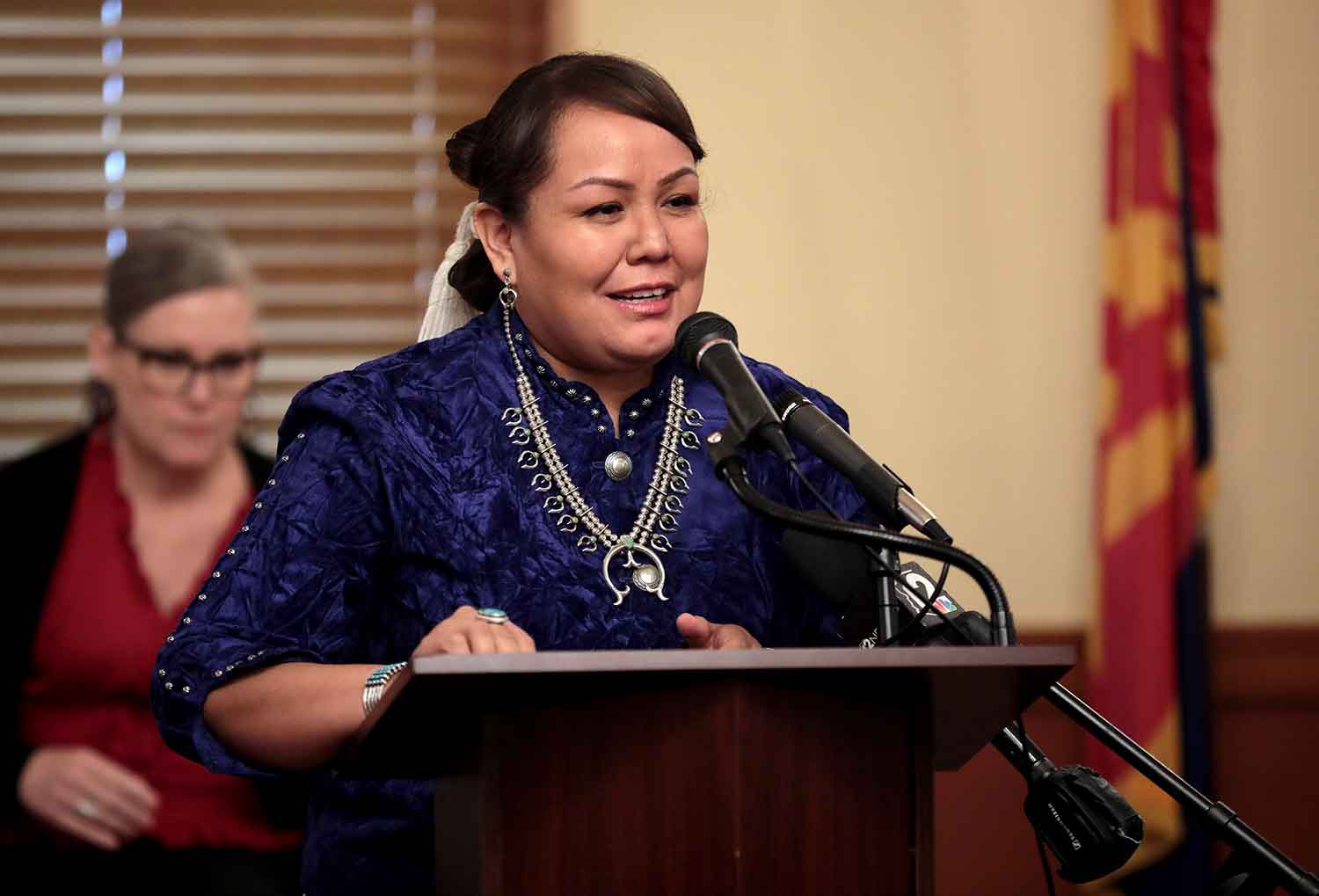 A woman speaks into a microphone at a podium.