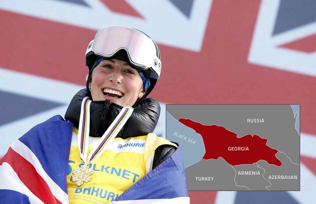 A young woman in snowboarding clothes and a medal around her neck smiles in front of the flag of Great Britain.