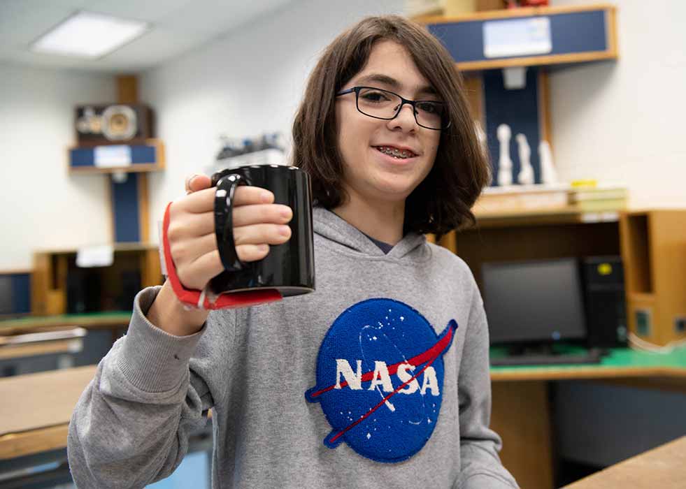 A teen with a device attached to his hand that is helping him grip a mug.