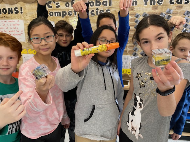 A group of students pose together holding vials, plastic cubes, and an EpiPen.