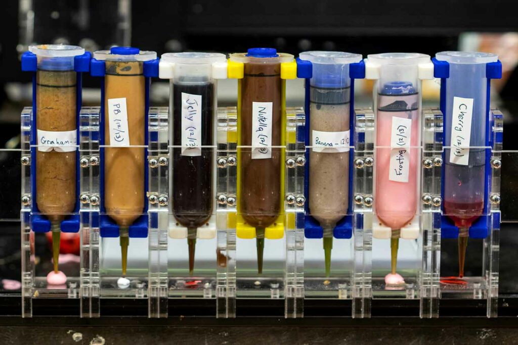 A printer part consisting of seven labeled tubes with different ingredients and narrow spouts at the bottom