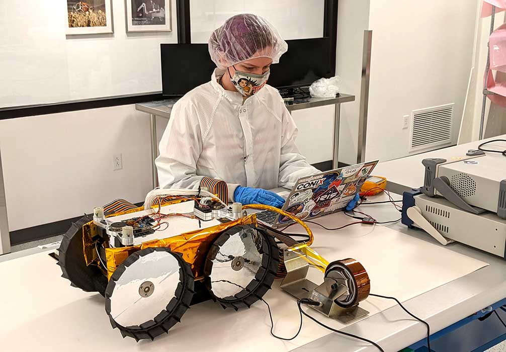 A student looks at a laptop that is on a table along with a rover.