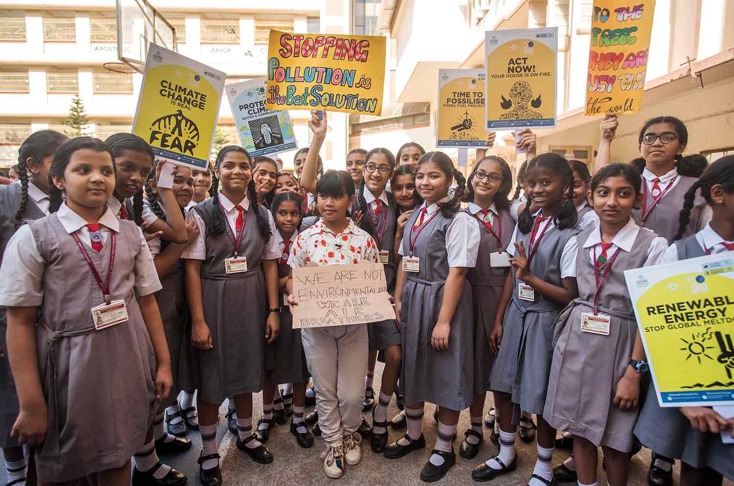 A young girl is surrounded by girls in school uniforms holding up signs supporting climate justice.