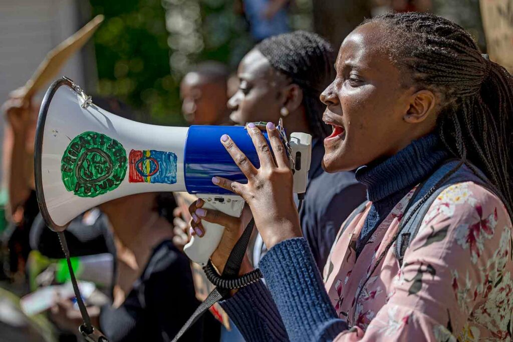 A young woman speaking into a megaphone with other activists in the background.