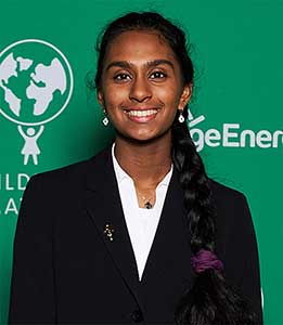 A young woman poses in front of a green background with a logo of a person holding up a planet.